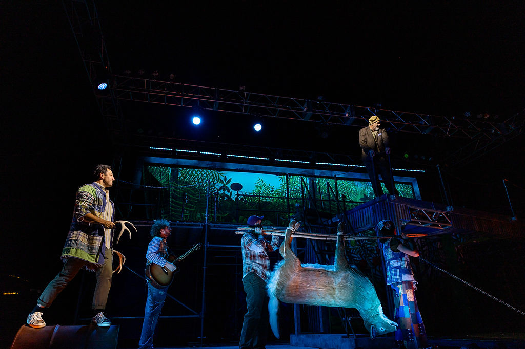 People on stage acting while a fake deer hangs upside down.