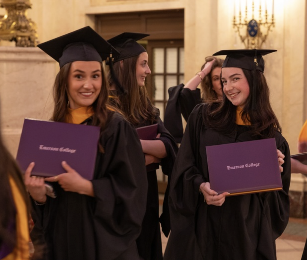 Two graduates smile while holding their diplomas