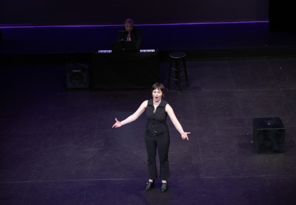 A woman sings with her arms open while on stage