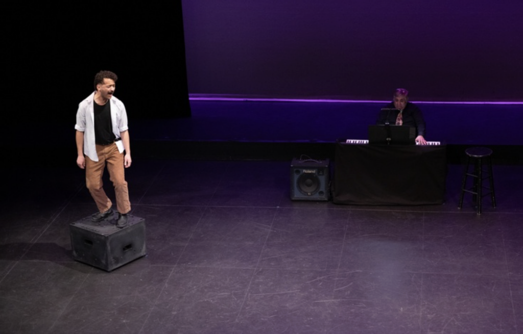 A man stands on a box while acting on stage