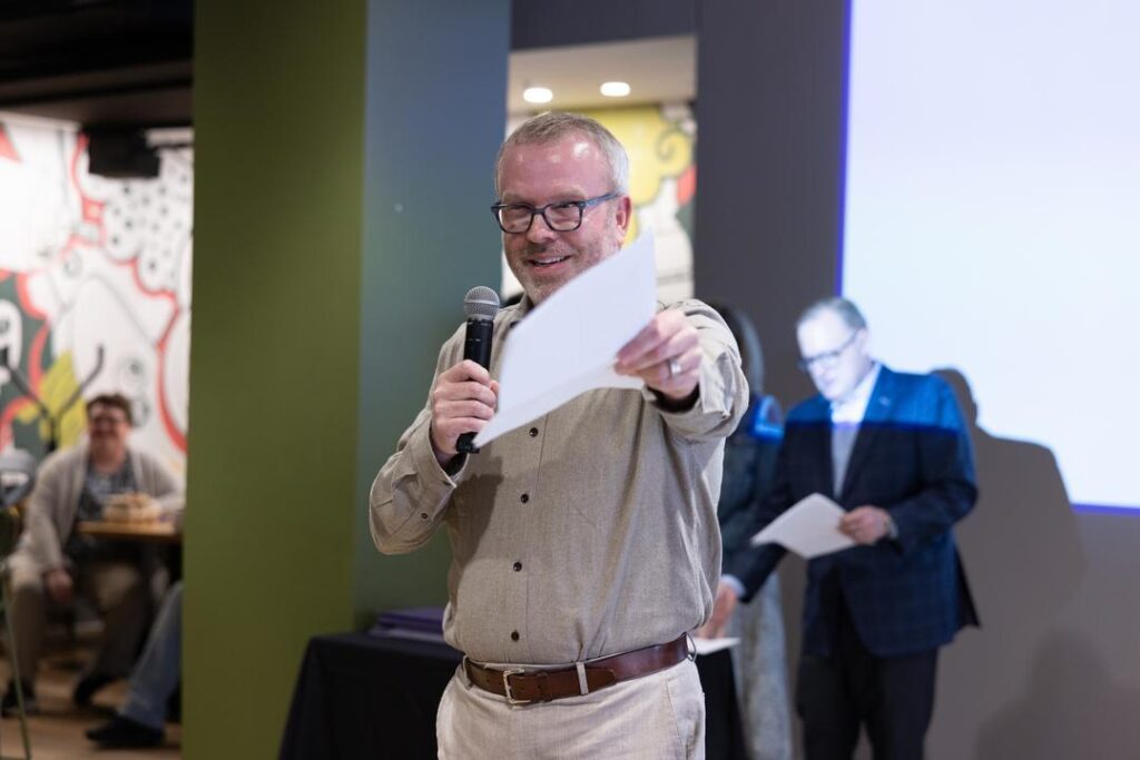 James Montgomery-Hyde looks at the camera while holding a mic and a piece of paper